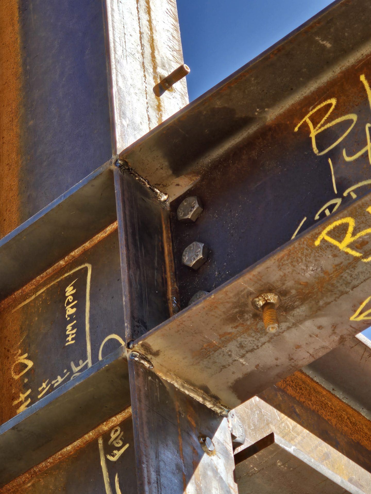 Close-up of a welded steel moment connection with weld-quality chalk markings