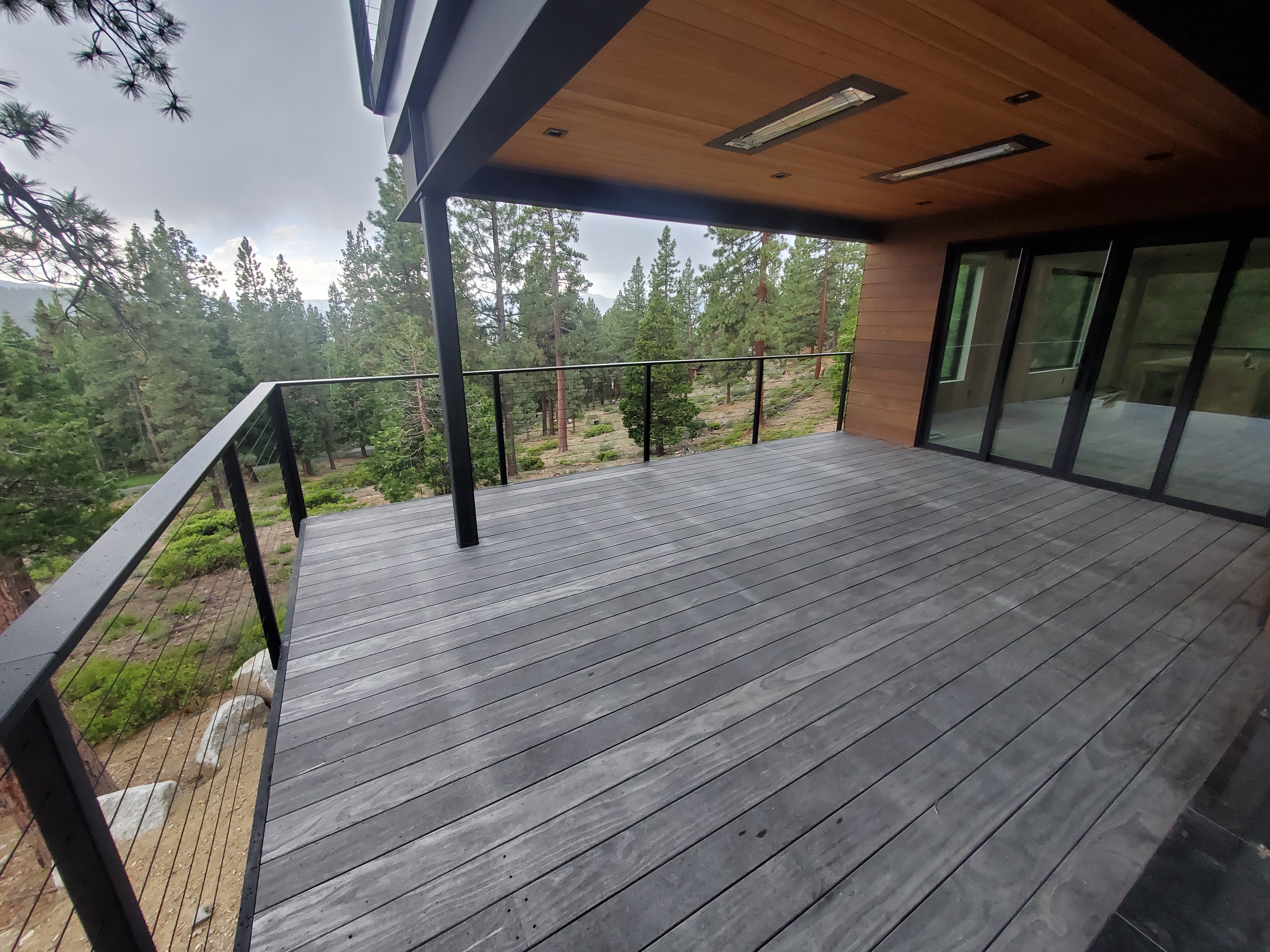 Long covered deck with custom black steel railing overlooking the forest at Bogowolski Residence